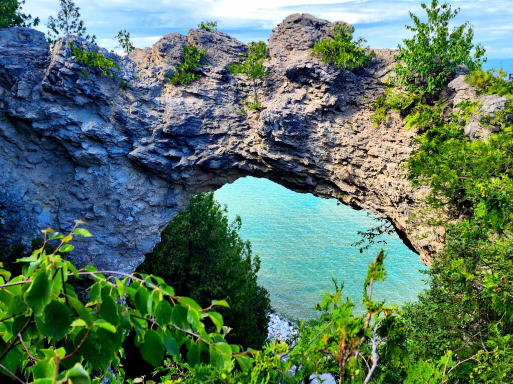 the crystal clear waters of lake Huron resting below Arch Rock, surrounded in lush greenery 