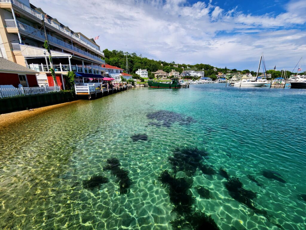 crystal clear water surrounding the ferry dock on Mackinac Island with colorful buildings lining the shore. 