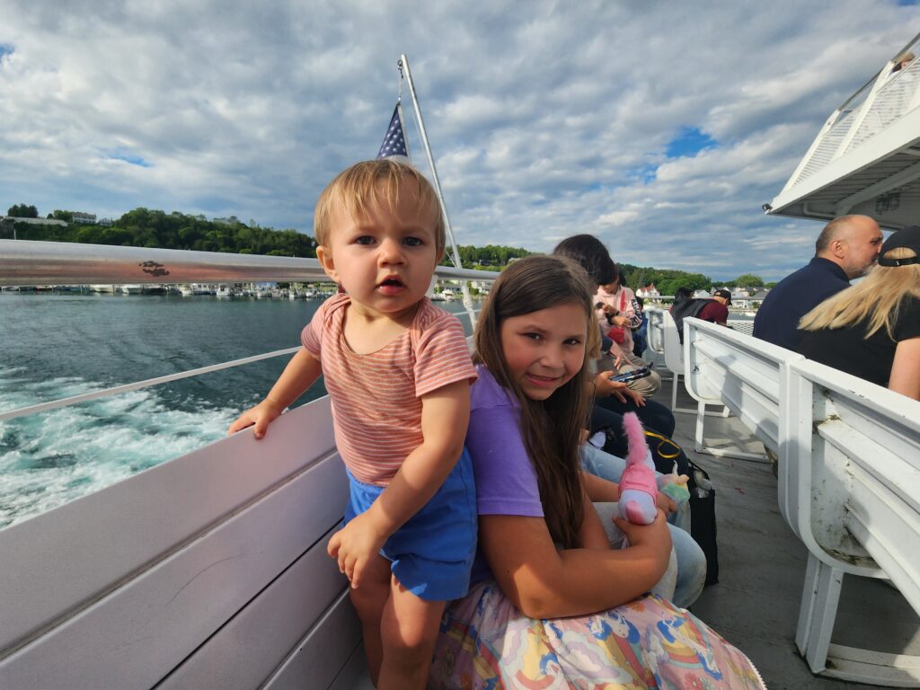 a baby boy and young girl sitting on a ferry bench with waves in the background. 