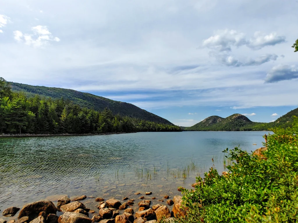 clear waters of Jordan pond in Acadia national park with mountains and lush greenery lining the background. 