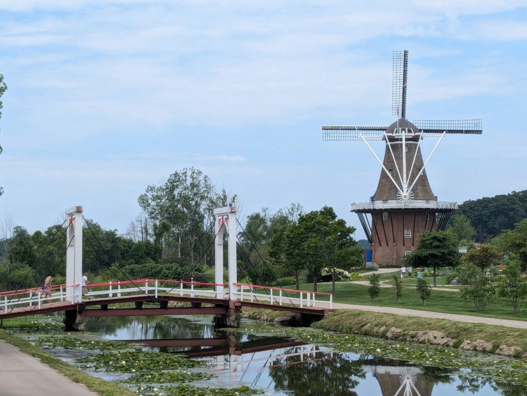 footbridge covering a small river with a brown, dutch inspired windmill in the background