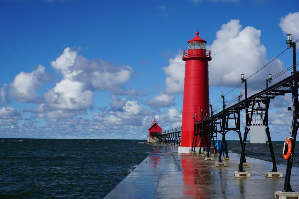 long black pier and bright red lighthouse against a cloudy blue sky