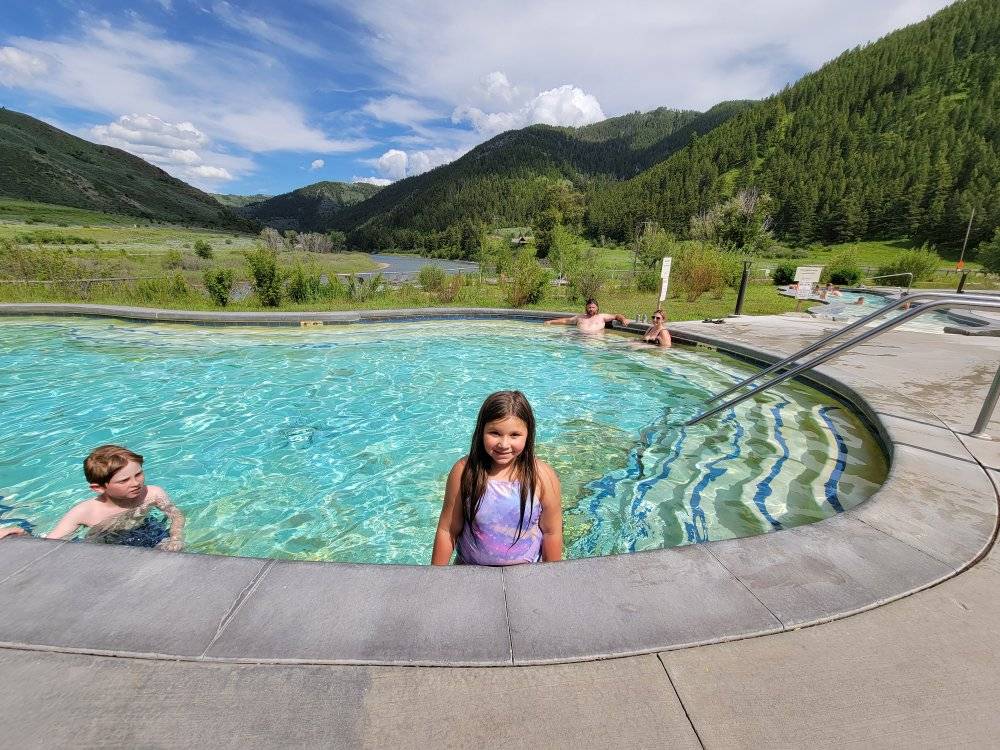 Kids enjoying a natural hot spring pool surrounded by mountains and river