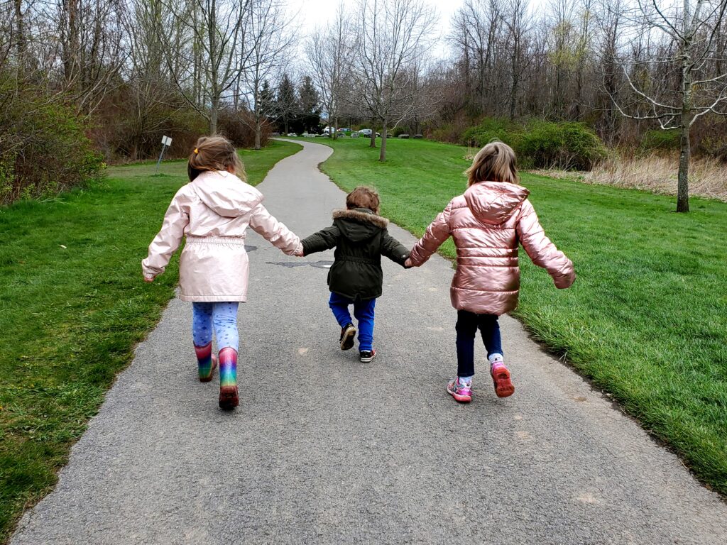 three young children walking along a paved path inside Chimney Bluffs State Park.