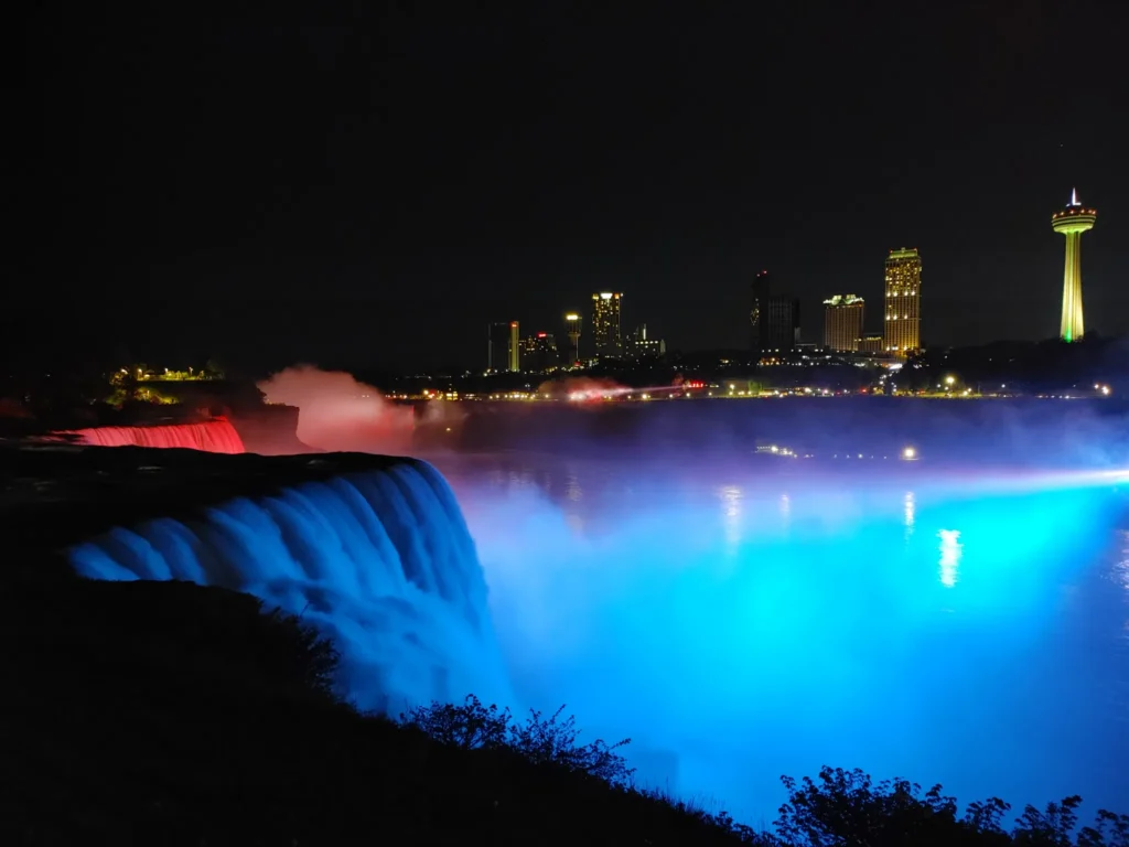 Blue and red lights shining on the American Falls with the Skylon Tower in the background, seeing the illumination is one of the best things to do in Niagara Falls 