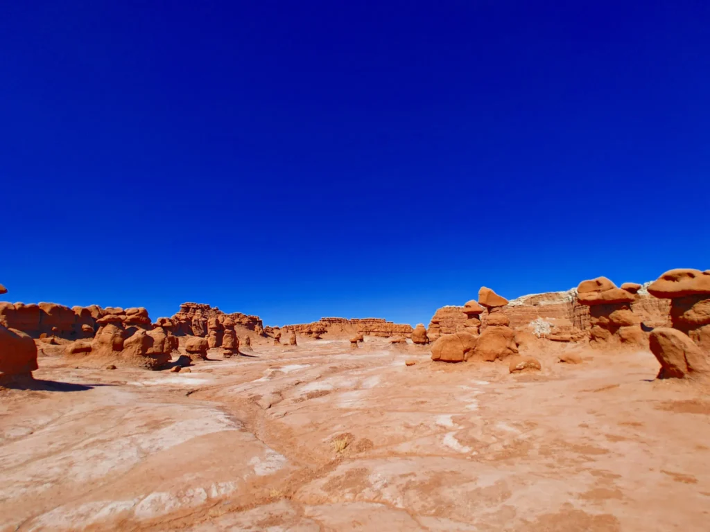 colorful hoodoos and cliffs in the distance inside Goblin valley State Park against a clear blue sky 