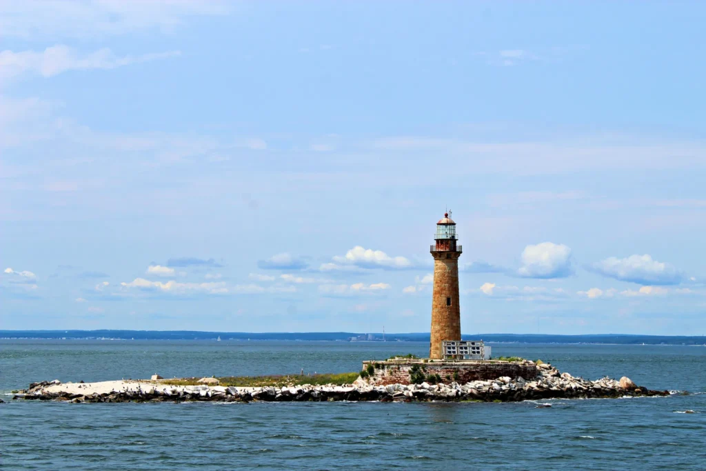 Little Gull Lighthouse standing on a rocky island surrounded by blue water under a cloudy sky.