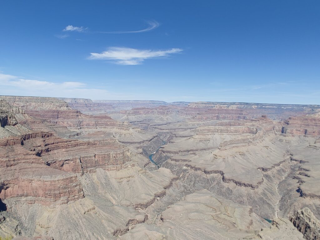 a distant view of a turquoise blue river cutting through the colorful cliffs of the grand canyon 