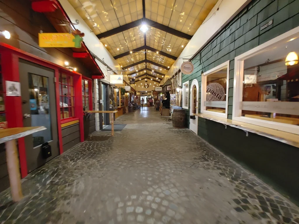 Indoor shopping walkway with cozy storefronts, cobblestone flooring, and warm lights at the Lake Placid Alpine Mall.
