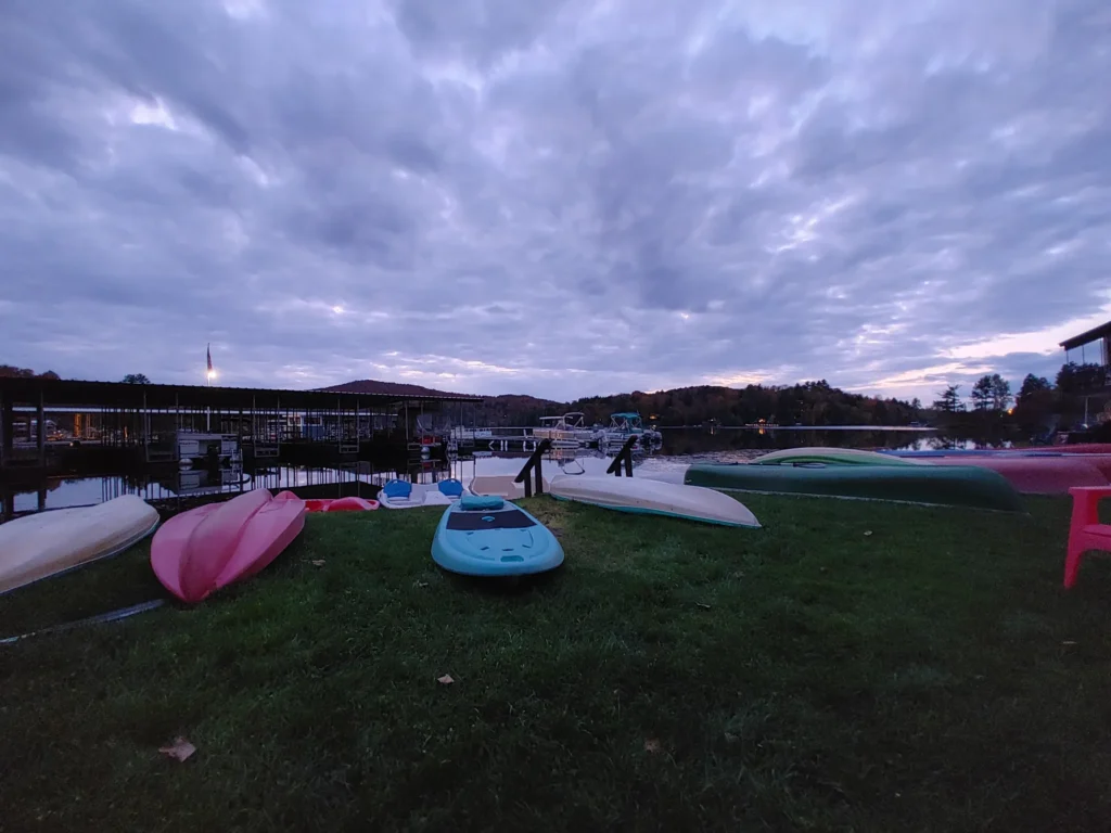 Kayaks and paddle boats lined along a lakeside marina at dusk, one of the relaxing attractions in Lake Placid.