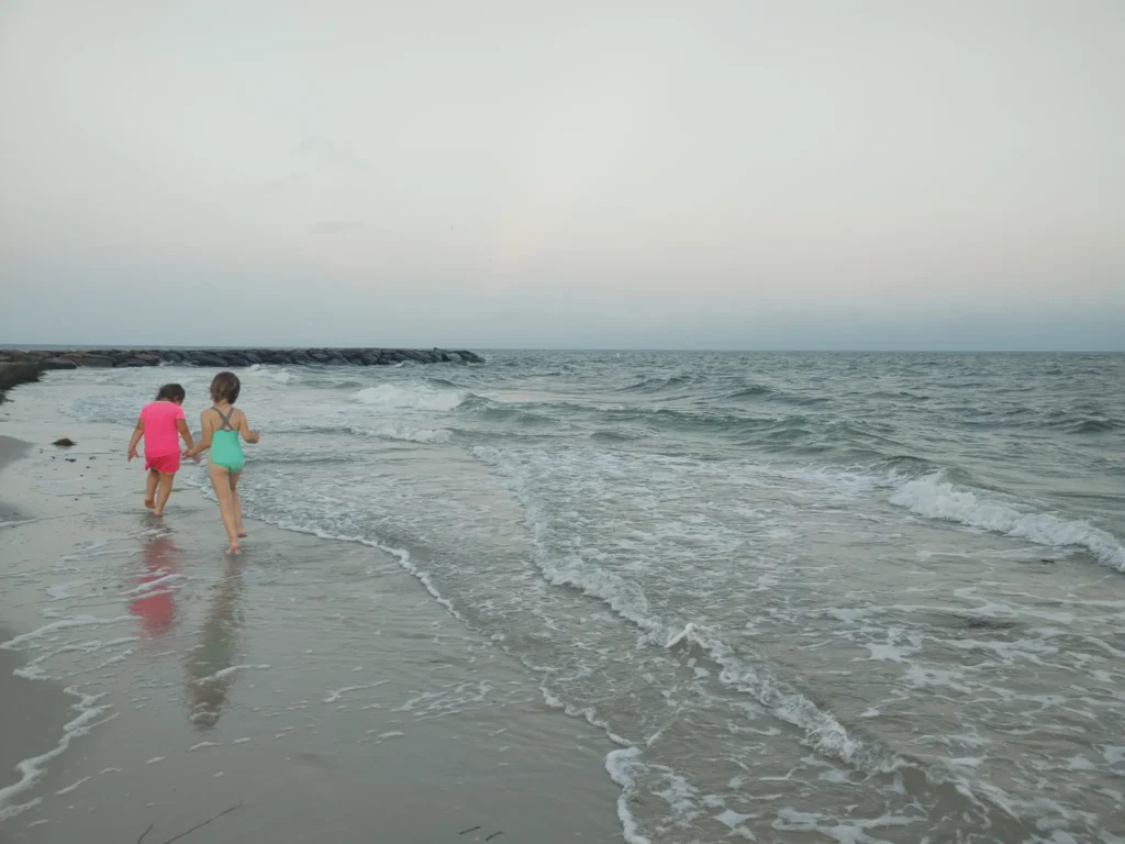 Two young girls walking along the coastline on Cape Cod, with waves crashing against the shore. 