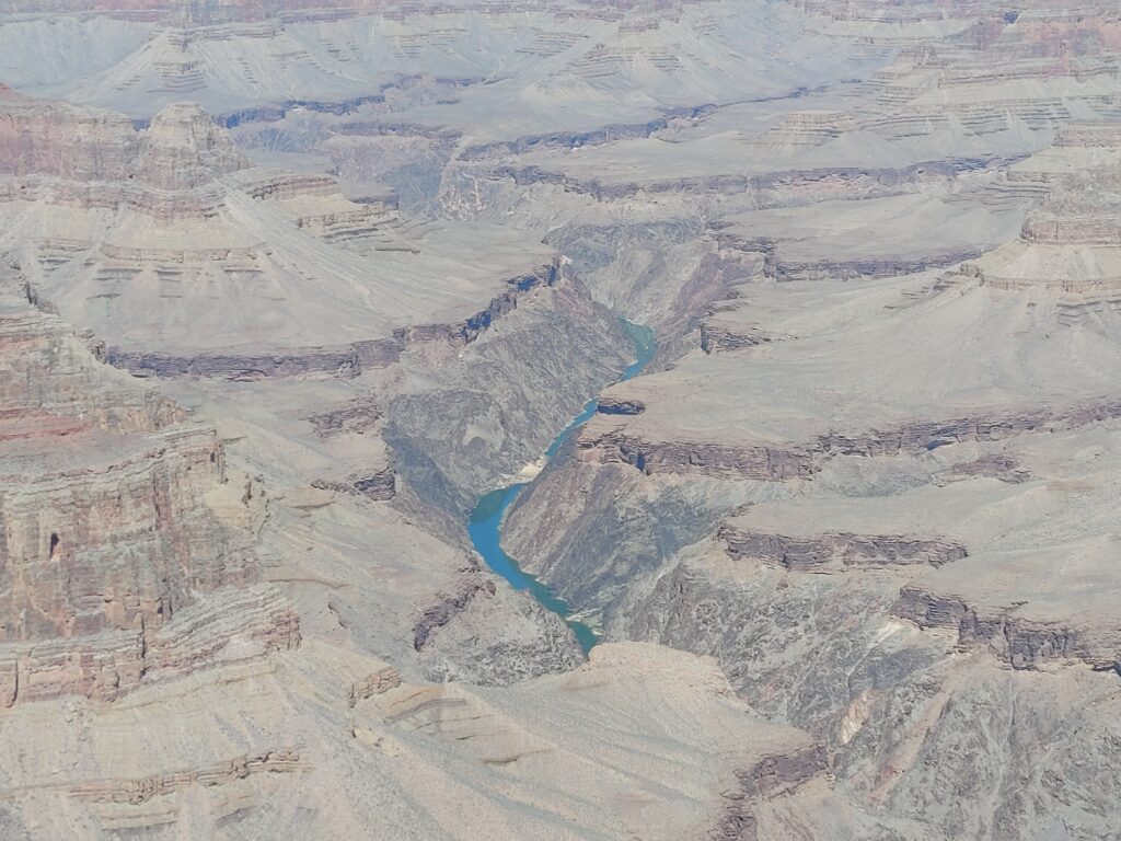 a turquoise blue river cutting through the cliffs of the grand canyon 