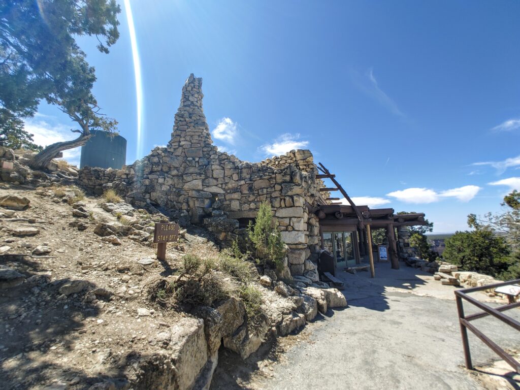 the stone structure of hermit's rest  from a gravel path, with a blue sky and fluffy clouds in the background. 