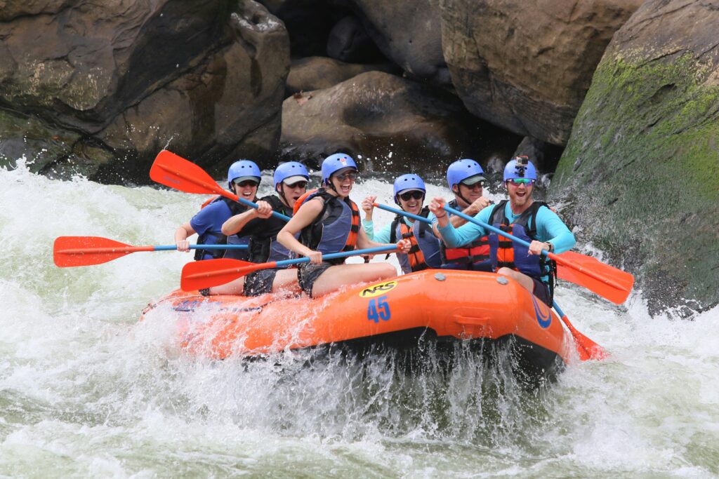 Family whitewater rafting through rocky rapids on a bright orange raft 