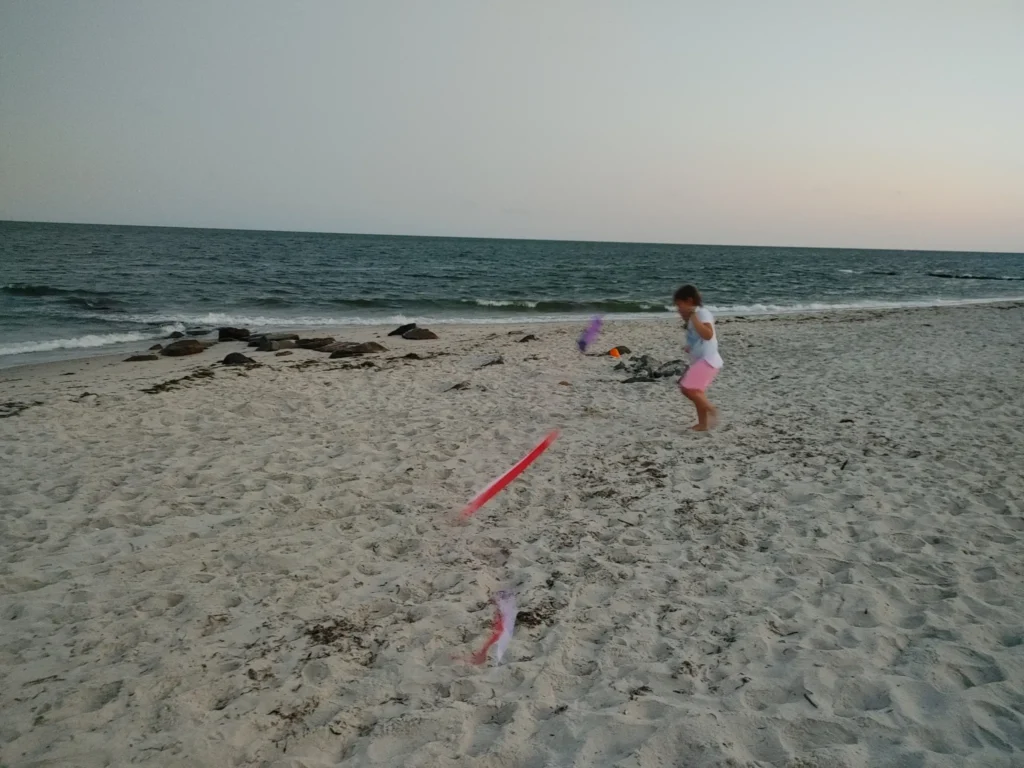 a young girl in pink shorts and a white t-shirt running on a Cape Cod beach while holding a kite 