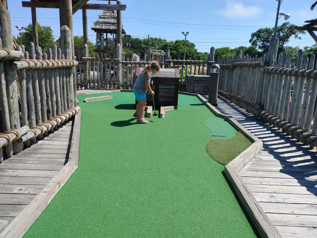 a young girl in blue shorts playing mini golf on a wooden boardwalks 