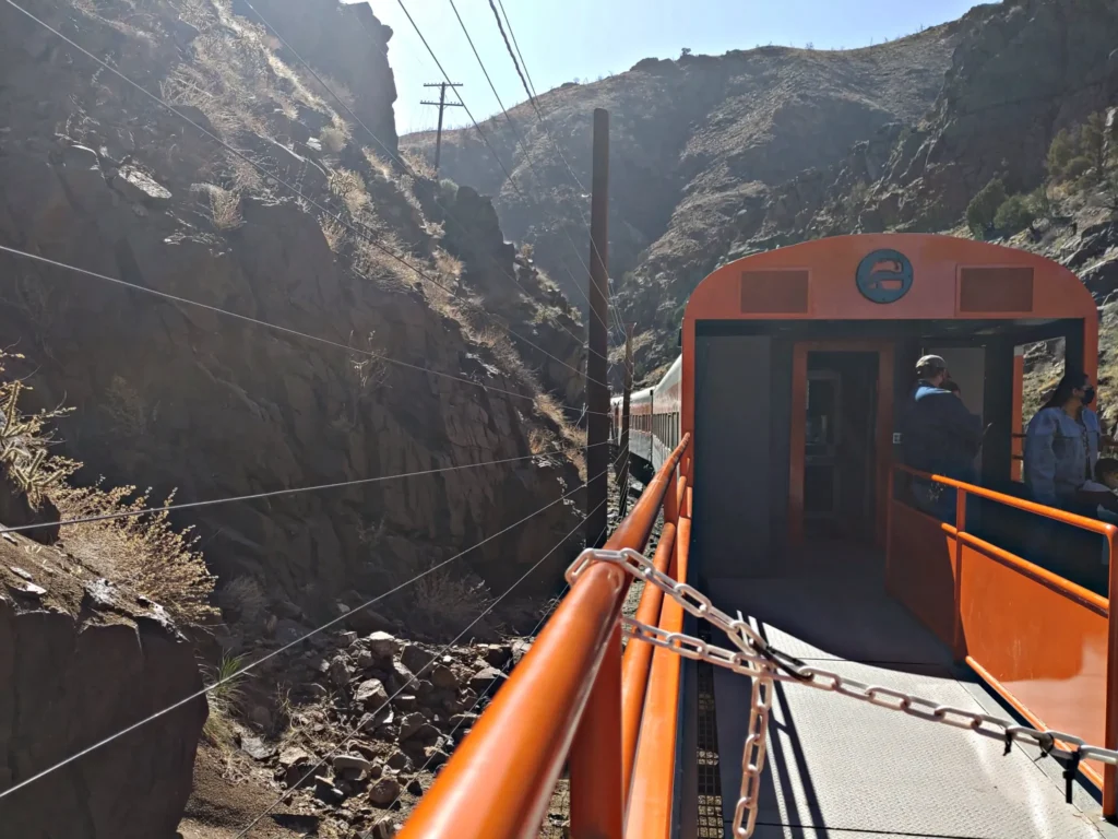 the orange painted open air cart of the Royal Gorge railroad with towering canyon cliffs 