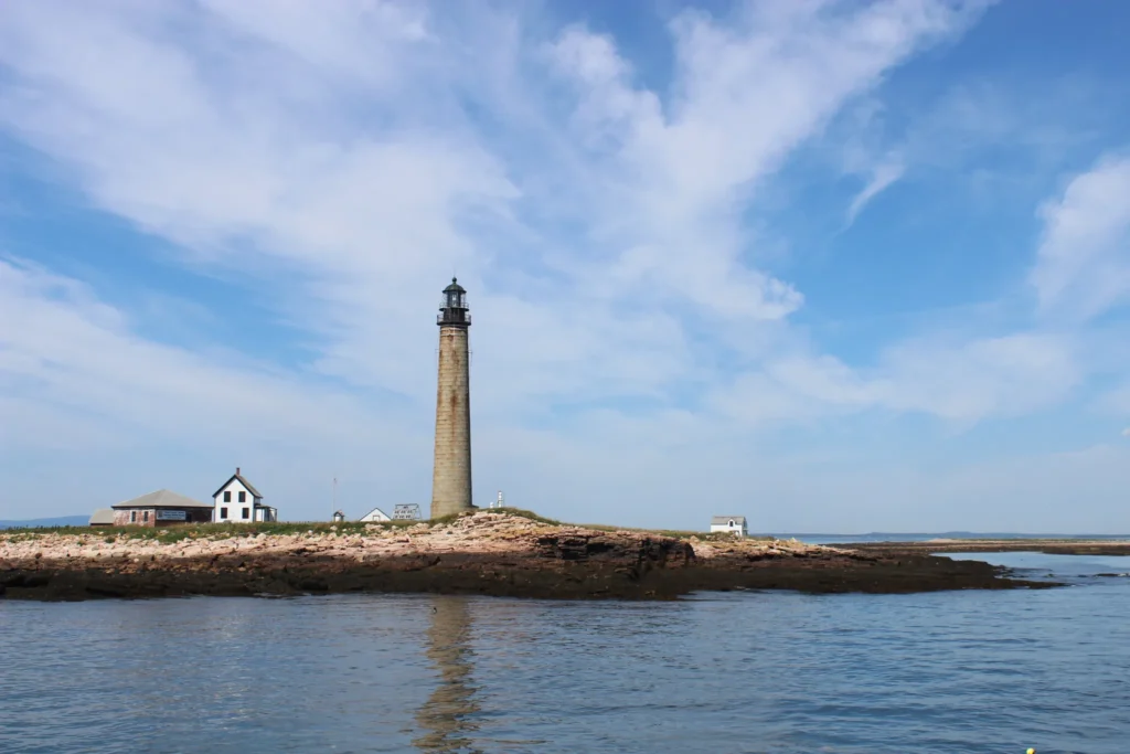 a tall brown lighthouse with a small white keepers house in the background, sitting on a small rocky island