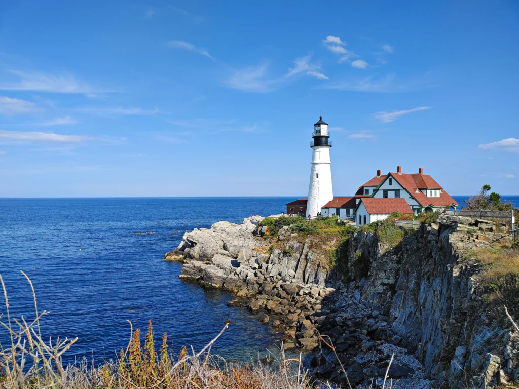 white lighthouse with keepers house with red roof at Portland Head lighthouse, one of the most popular Maine lighthouses