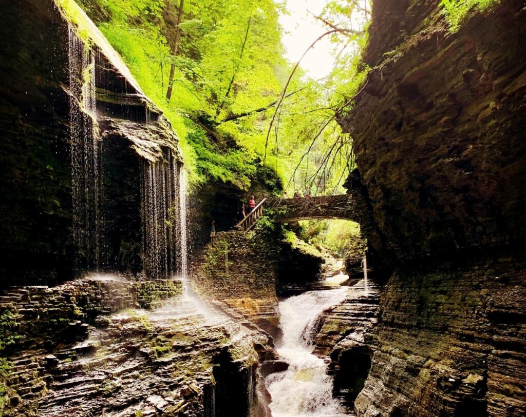 Waterfall flowing through a rocky gorge beneath a small stone bridge.
