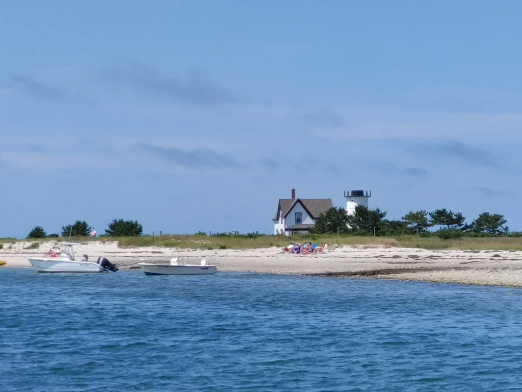 the white keepers house and Stage Harbor lighthouse on the tip of cape cod with the blue water ocean in the foreground. 