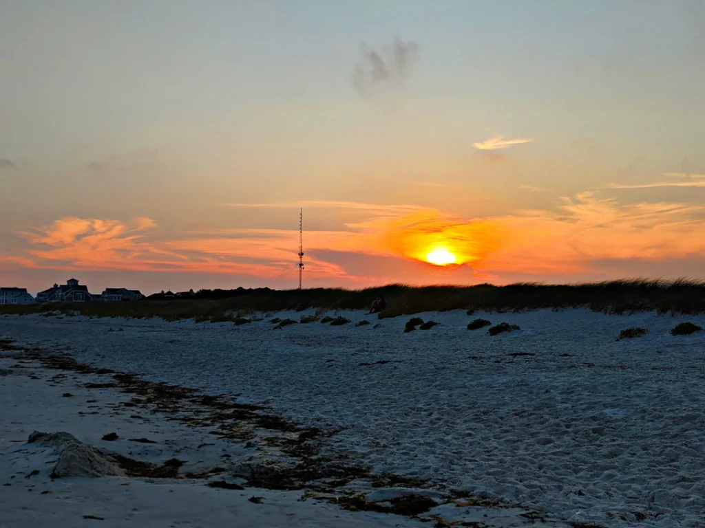 orange and pink swirls in the sky with a sandy beach foreground in Cape Cod 