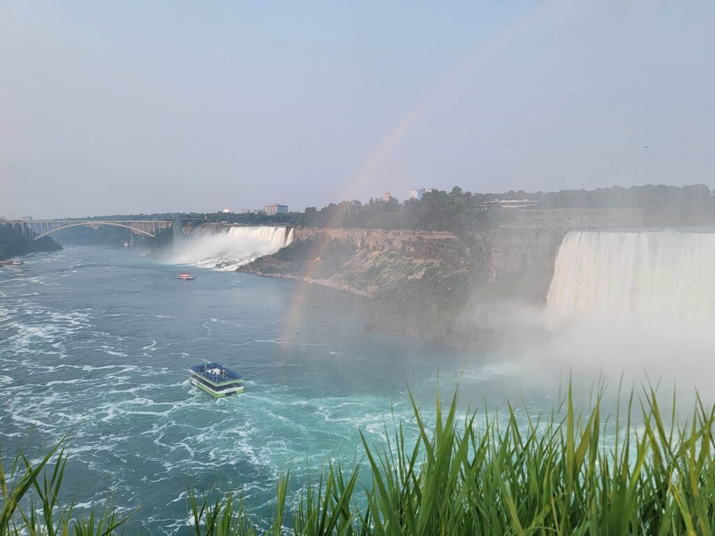 Rainbow arches over Niagara Falls as a tour boat cruises through the mist below the American Falls and Horseshoe Falls.