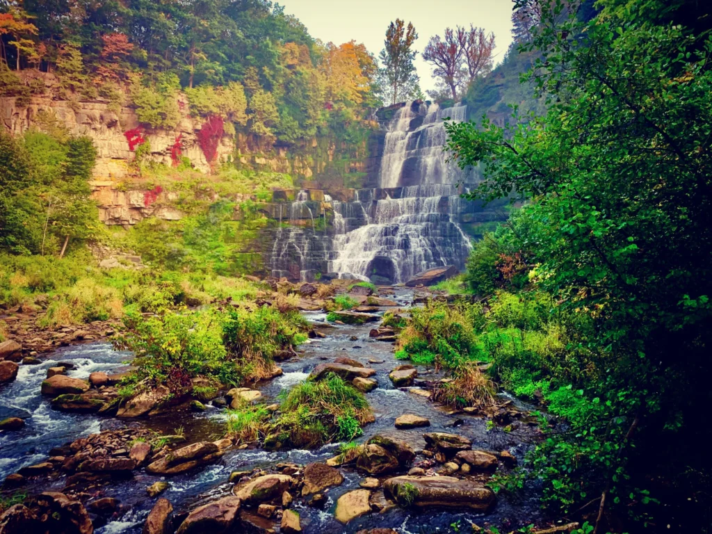 Chittenango Falls cascading over rocky cliffs surrounded by colorful forest scenery.