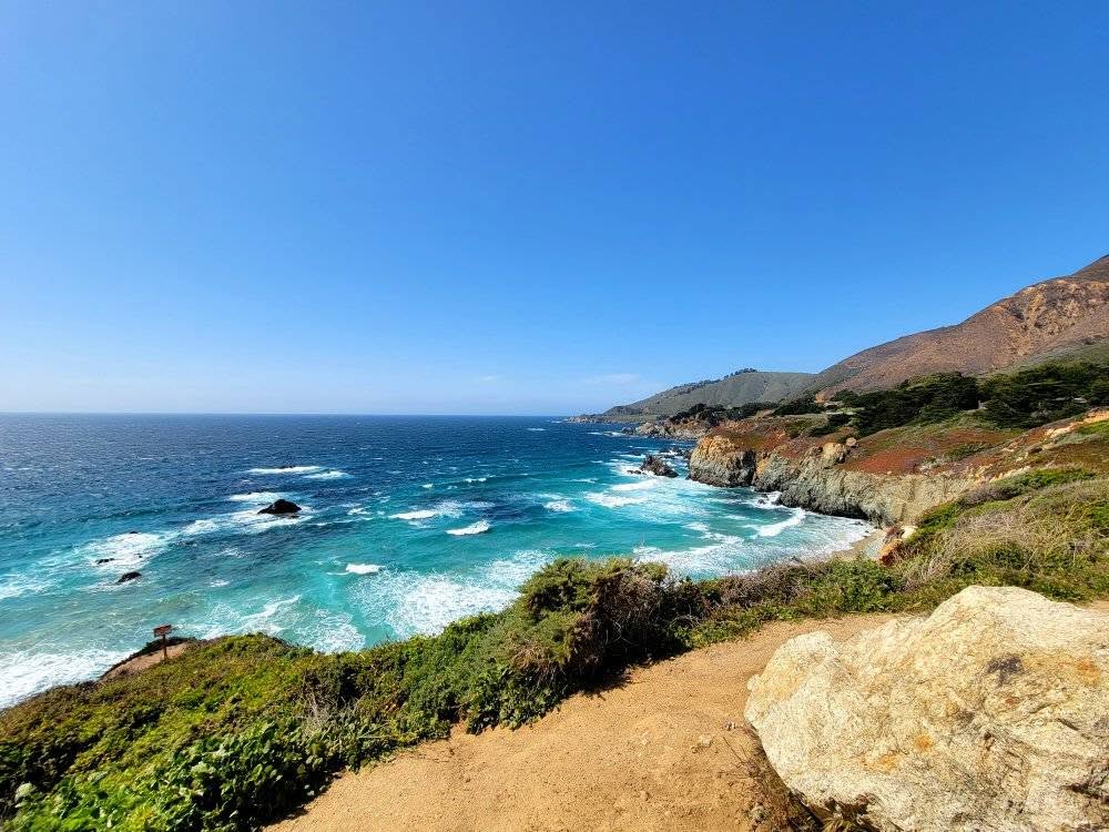 Big Sur coastline with turquoise waves, rocky cliffs, and a scenic coastal trail.