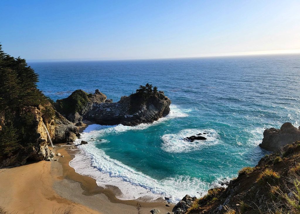 McWay Falls cascading onto a sandy beach along the Big Sur coastline.