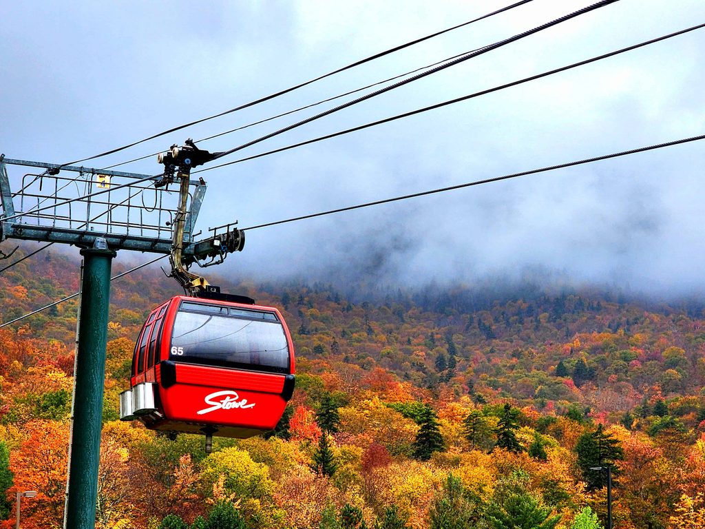 Red gondola traveling over colorful fall foliage in the mountains, one of the best October bucket list activities