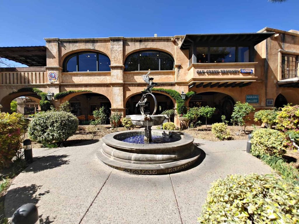 a fountain sitting in a plaza surrounded by green plants and bushes in the Tlaquepaque Arts and Craft Village