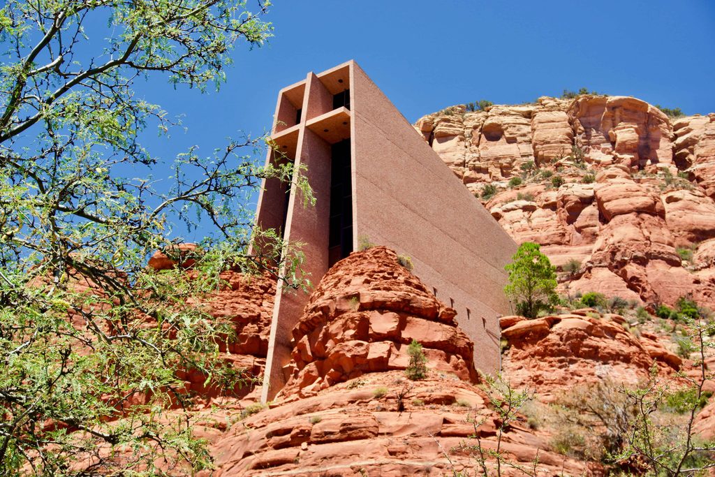the chapel of the holy cross building extending out of sedona's red rocks with lush greenery in the foreground 